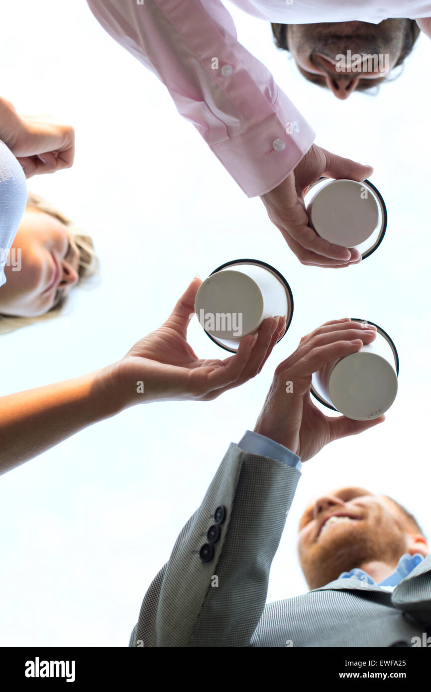Directly below shot of businesspeople holding disposable cups against clear sky Stock Photo