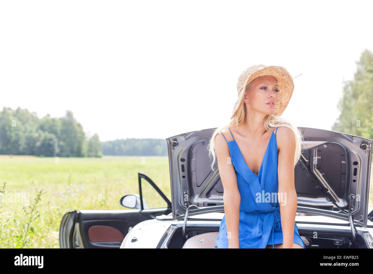 Woman looking away while sitting on convertible trunk against clear sky Stock Photo