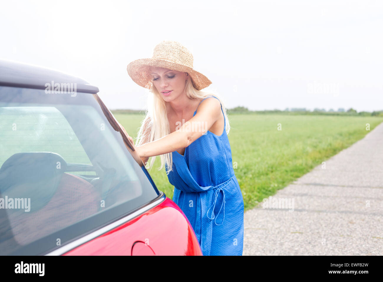 Woman pushing broken down car on country road against clear sky Stock Photo