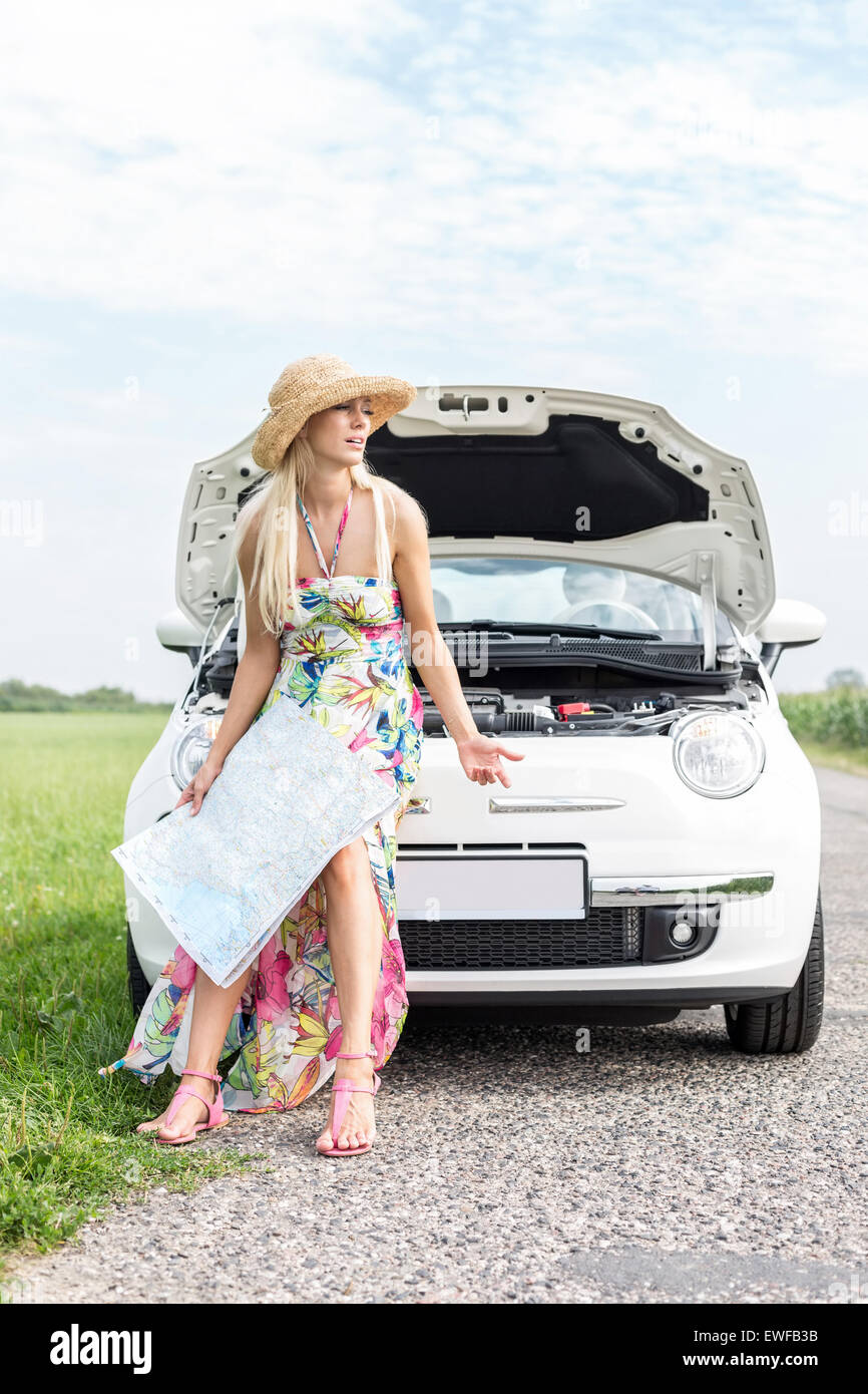 Frustrated woman with map sitting on broken down car Stock Photo