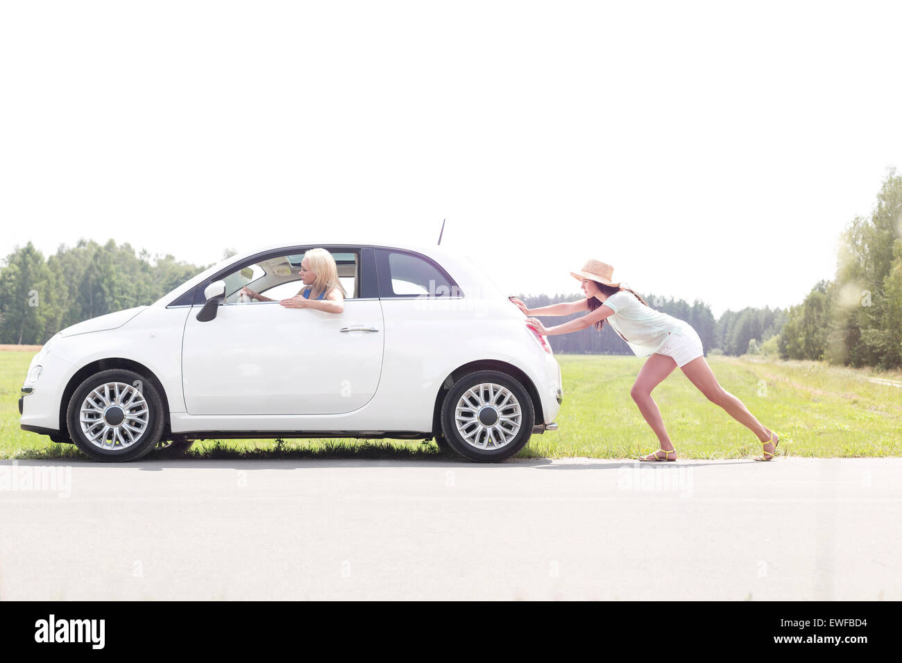 Woman pushing broken down car on country road Stock Photo
