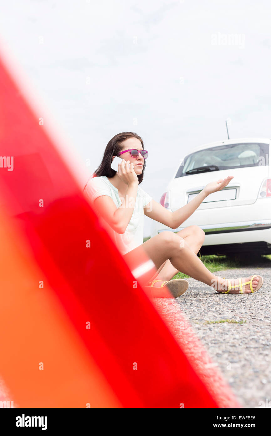 Frustrated woman using cell phone while sitting by broken down car Stock Photo