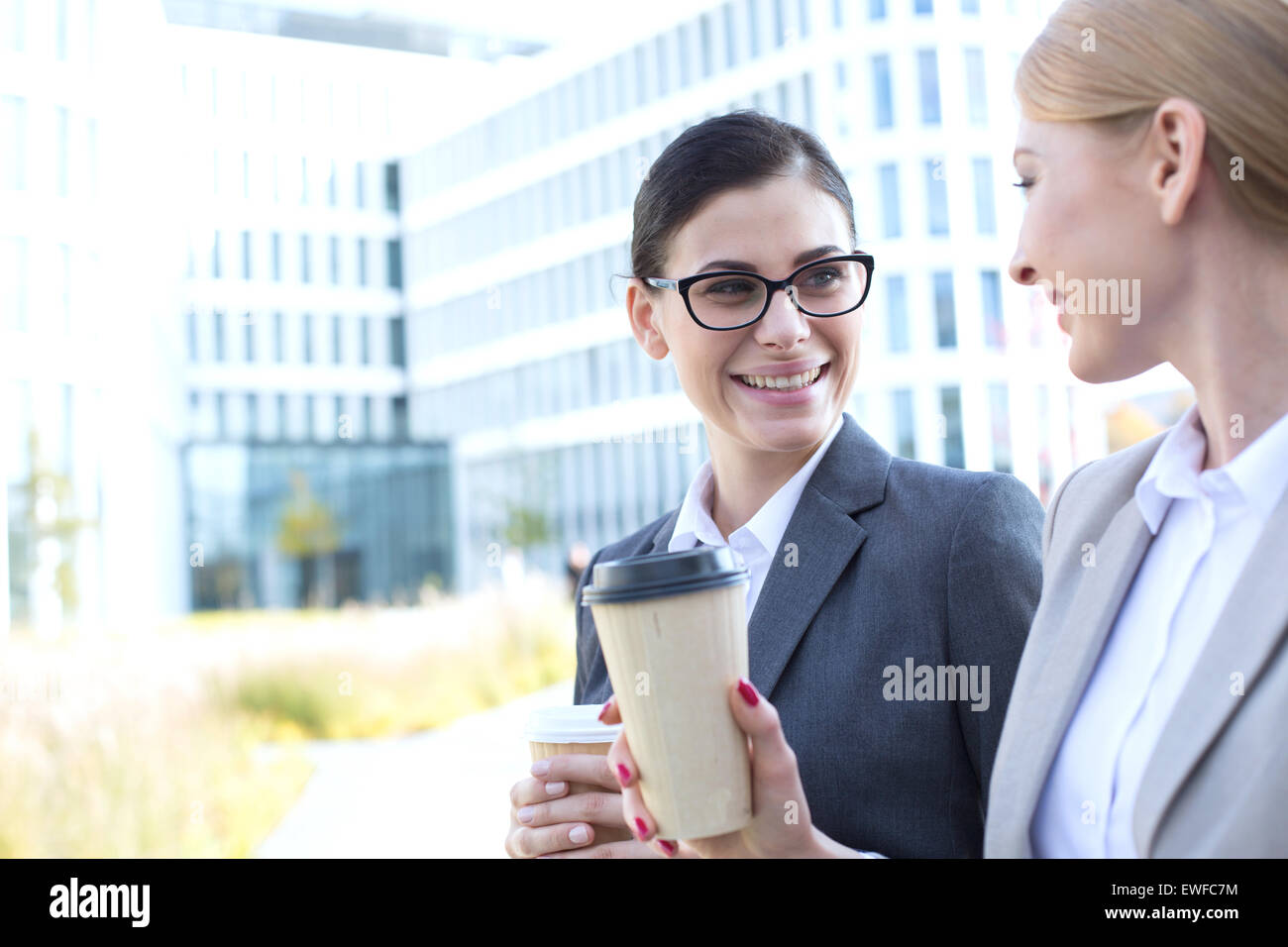 Two businesswomen holding disposable cups smiling hires stock