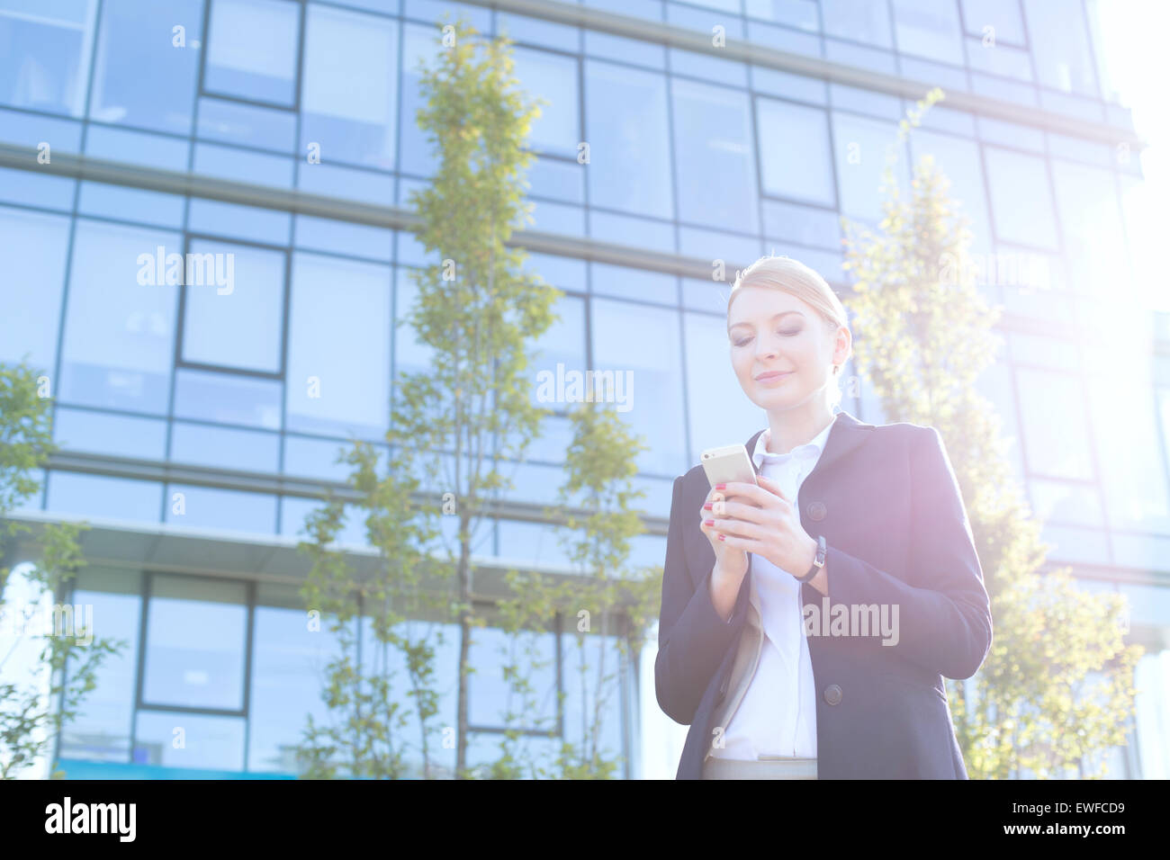 Businesswoman text messaging through cell phone on sunny day Stock Photo