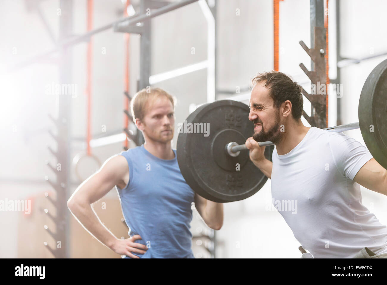 Man assisting friend in lifting barbell at crossfit gym Stock Photo