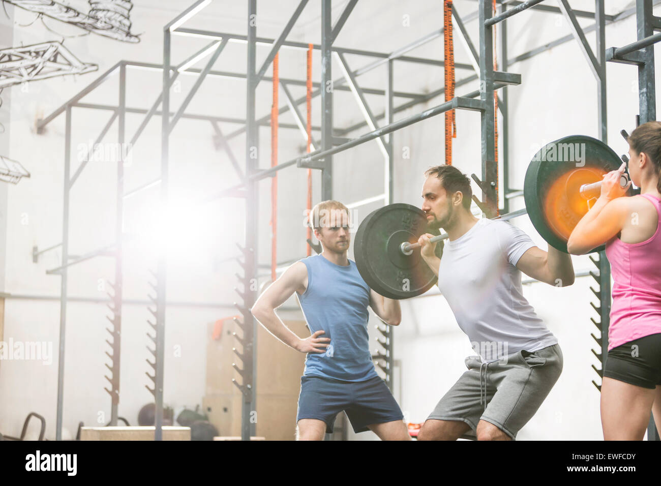People assisting man in lifting barbell at crossfit gym Stock Photo