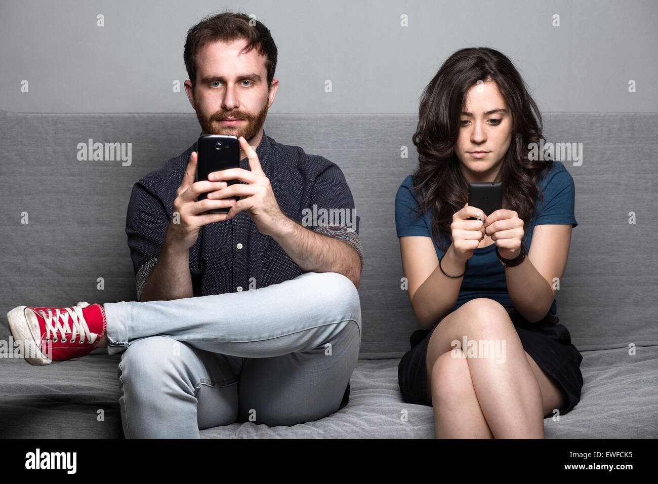 Young Silent Couple with Smartphones Sitting on a Couch Stock Photo