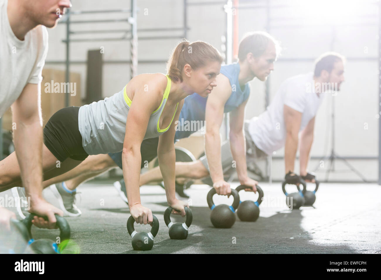 Determined people doing pushups with kettlebells at crossfit gym Stock Photo