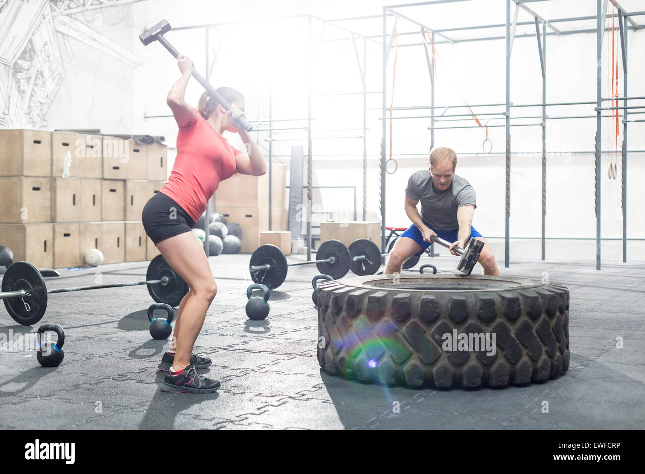 Dedicated man and woman hitting tire with sledgehammer in crossfit gym Stock Photo