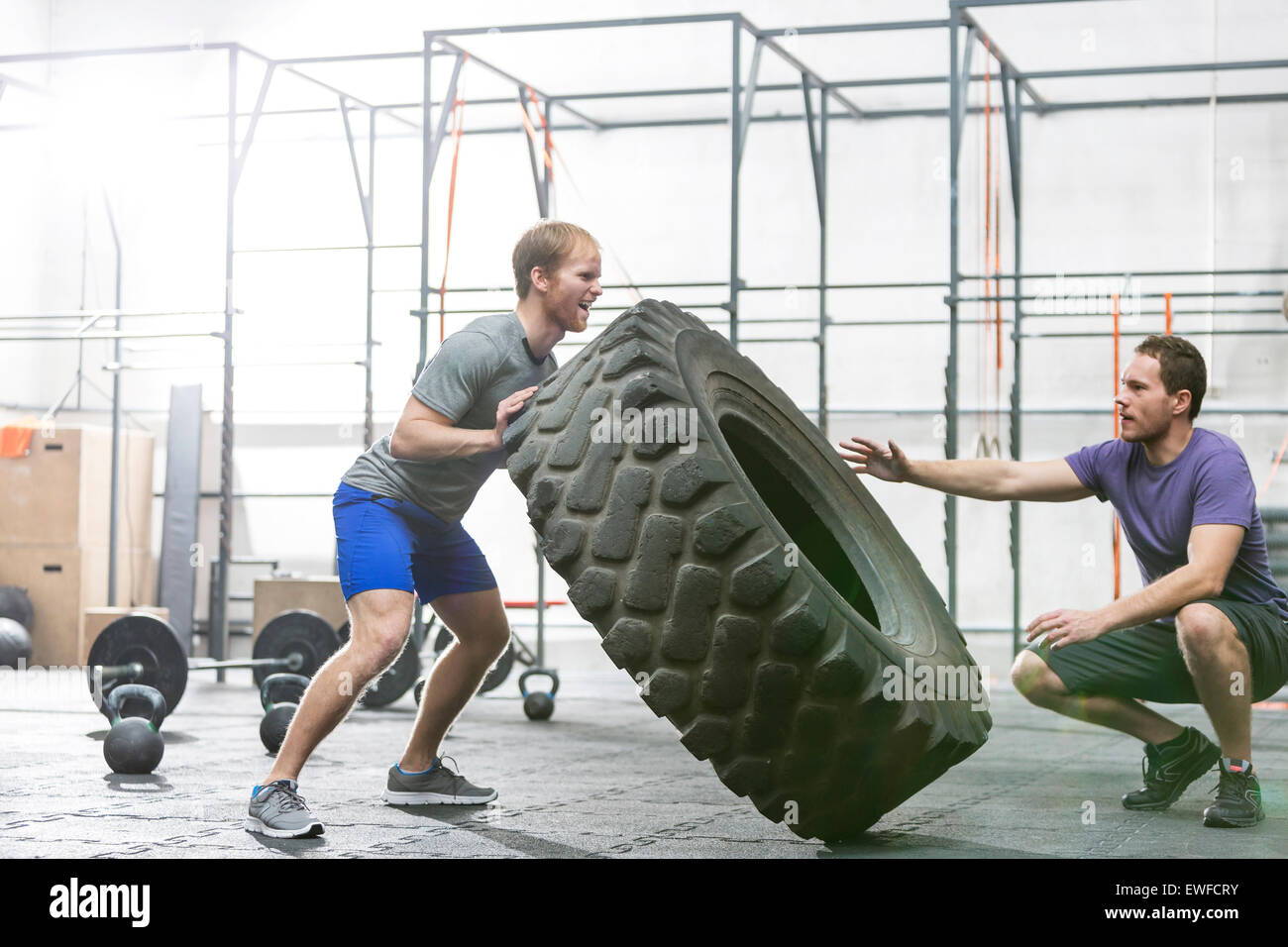 Man assisting at dedicated friend in flipping tire at crossfit gym Stock Photo