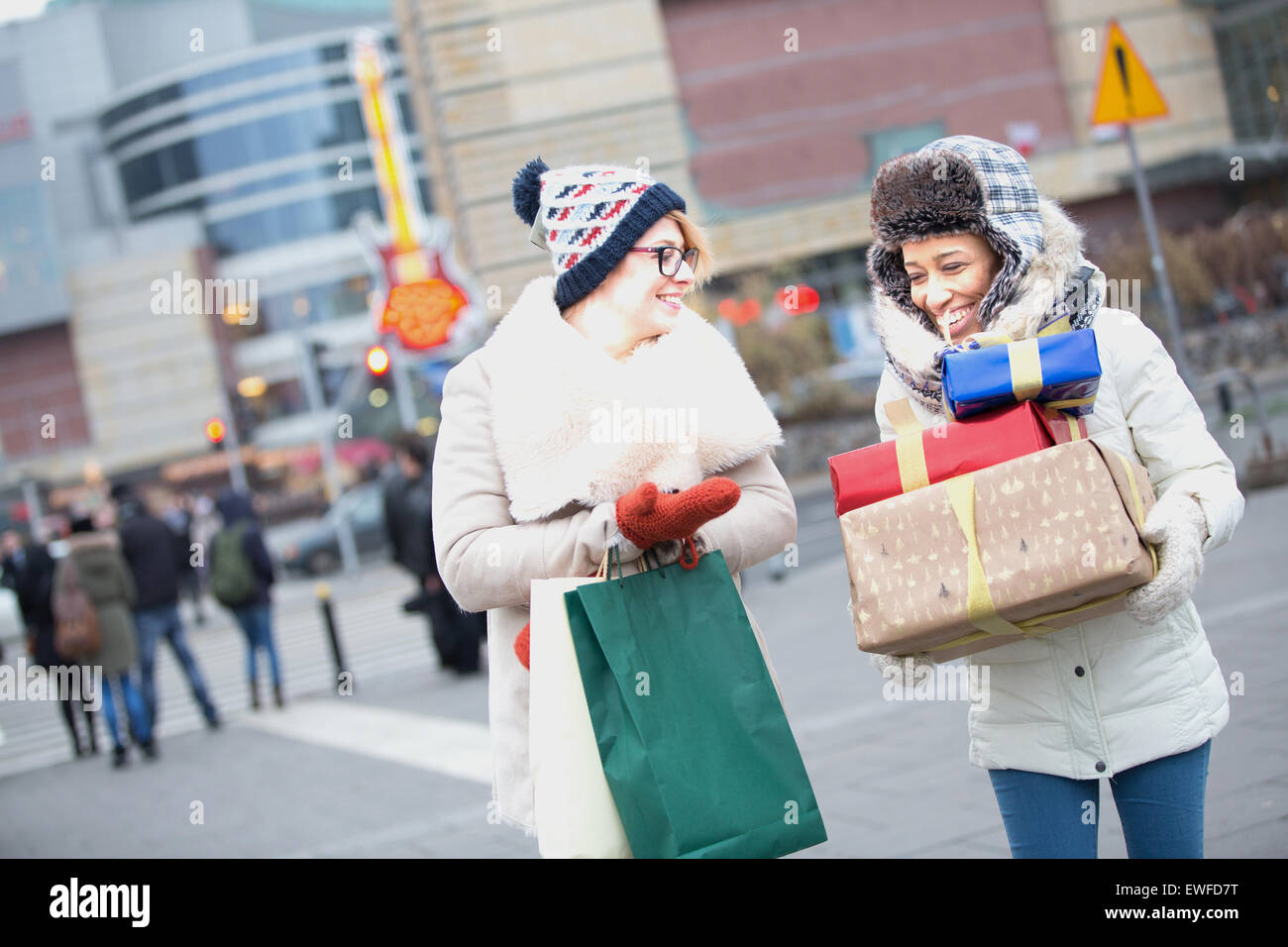 Happy women with gifts and shopping bags walking on city street during winter Stock Photo