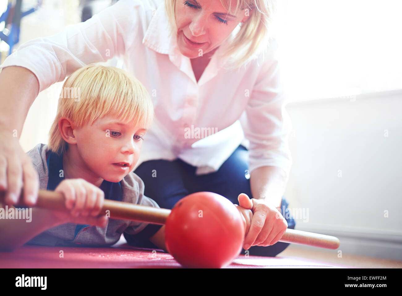 Physical therapist guiding boy rolling ball with stick Stock Photo
