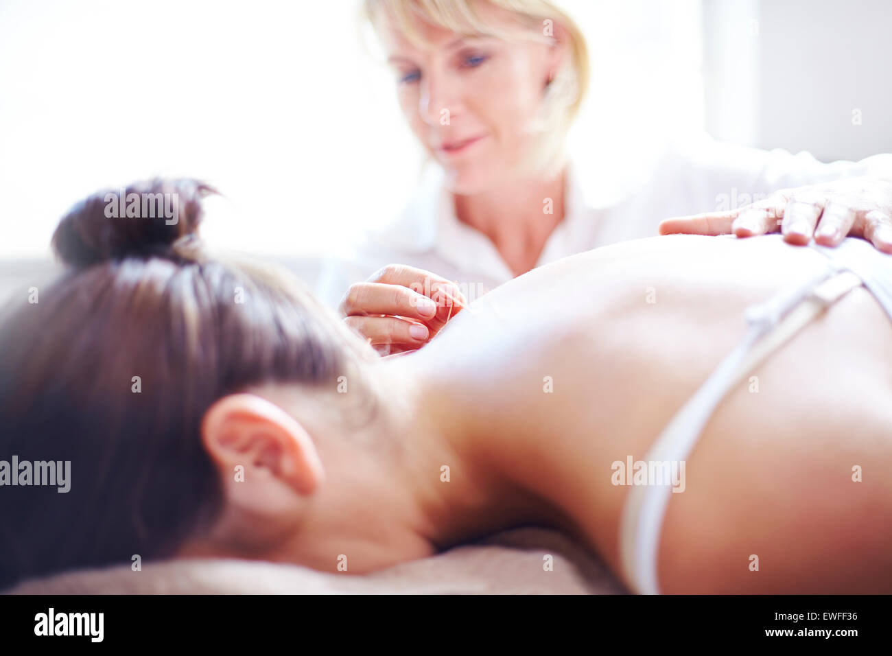 Acupuncturist applying acupuncture needle to woman’s neck Stock Photo