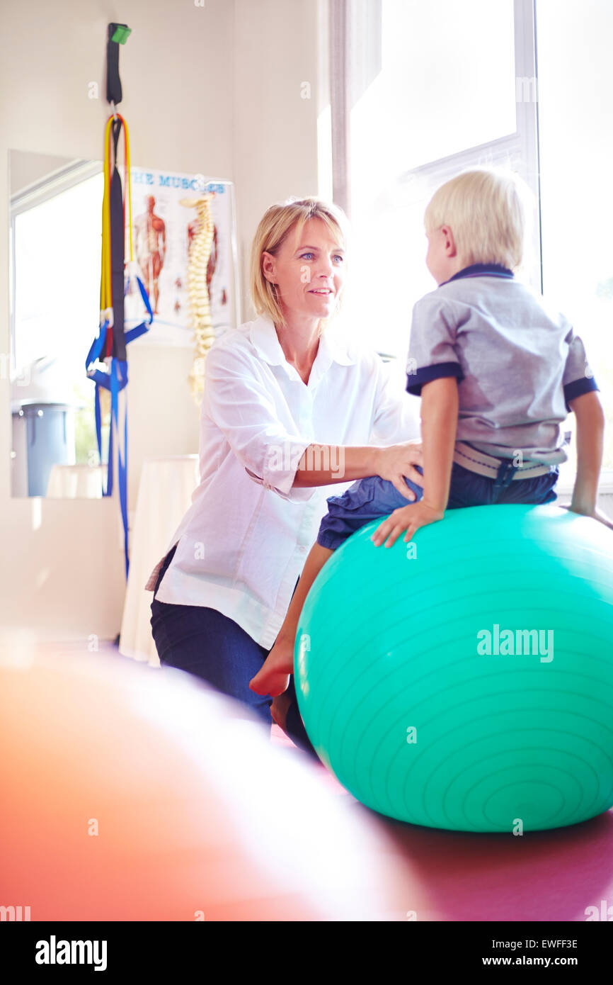 Physical therapist holding boy on fitness ball Stock Photo