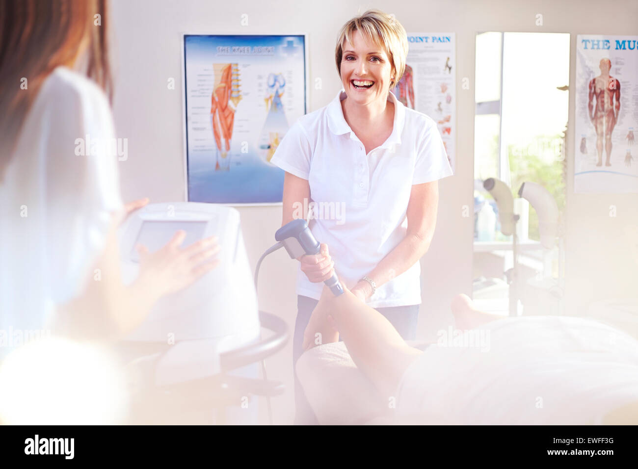 Smiling physical therapist using ultrasound probe on patient’s leg Stock Photo