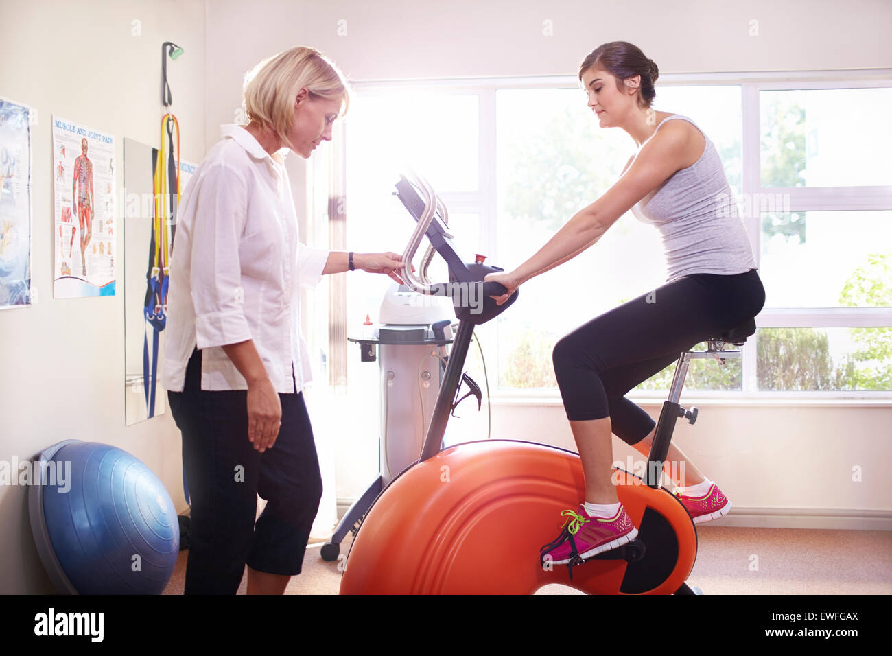 Physical therapist guiding woman on stationary bike Stock Photo