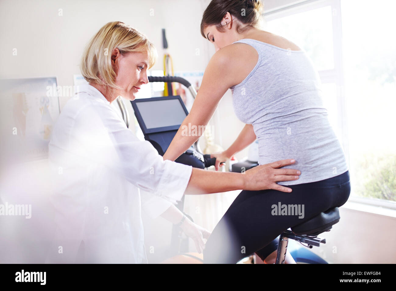 Physical therapist guiding woman’s hips on stationary bike Stock Photo