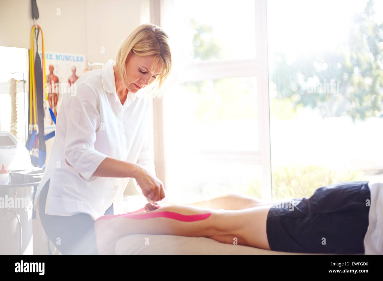 Physical therapist applying kinesiology tape to man’s leg Stock Photo