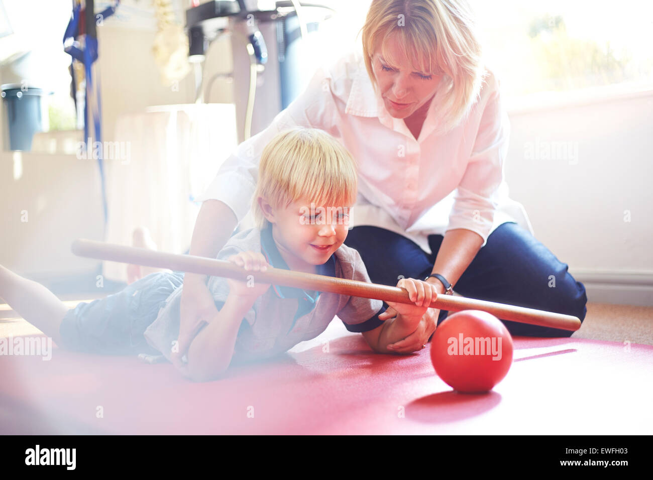 Physical therapist guiding boy rolling ball with stick Stock Photo