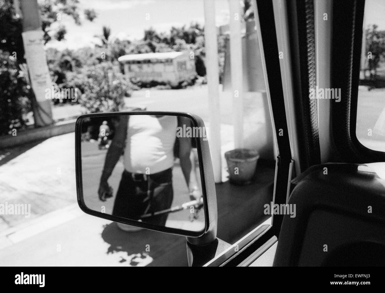 Reflection of a petrol attendant in a wing mirror with an abandoned bus in the distance, Mauritius. Stock Photo