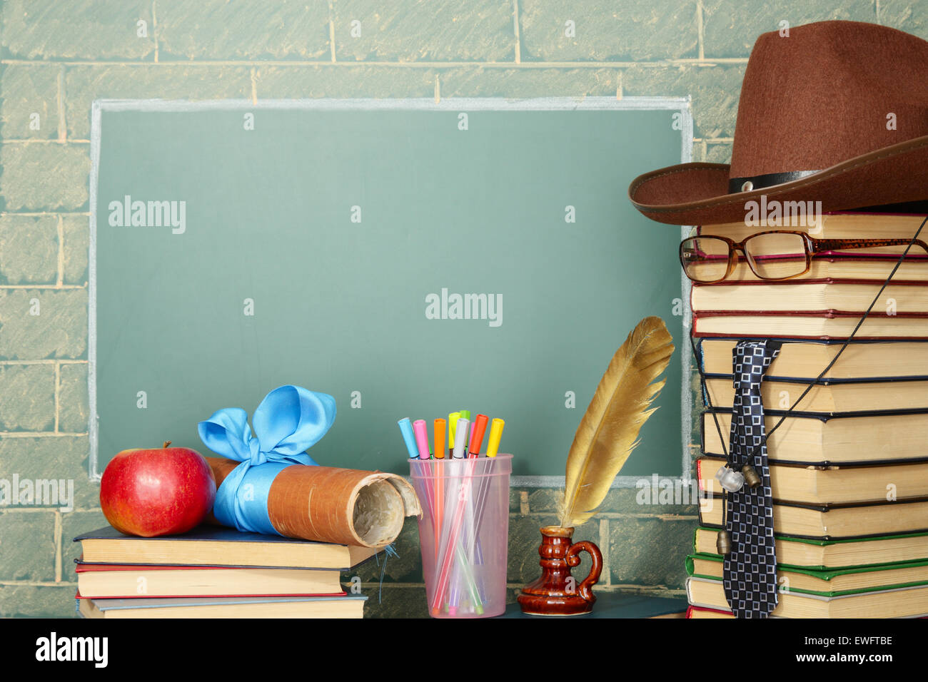 Unusual jesting teacher, books, quill, pen, scroll, apple before blackboard with copy space Stock Photo