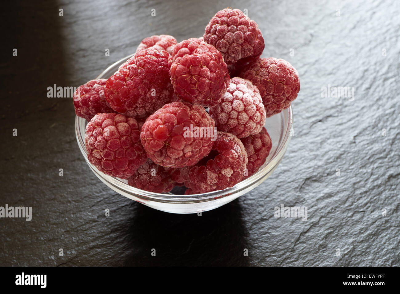 Macro shot of some frozen raspberries in a glass bowl on a slate ...