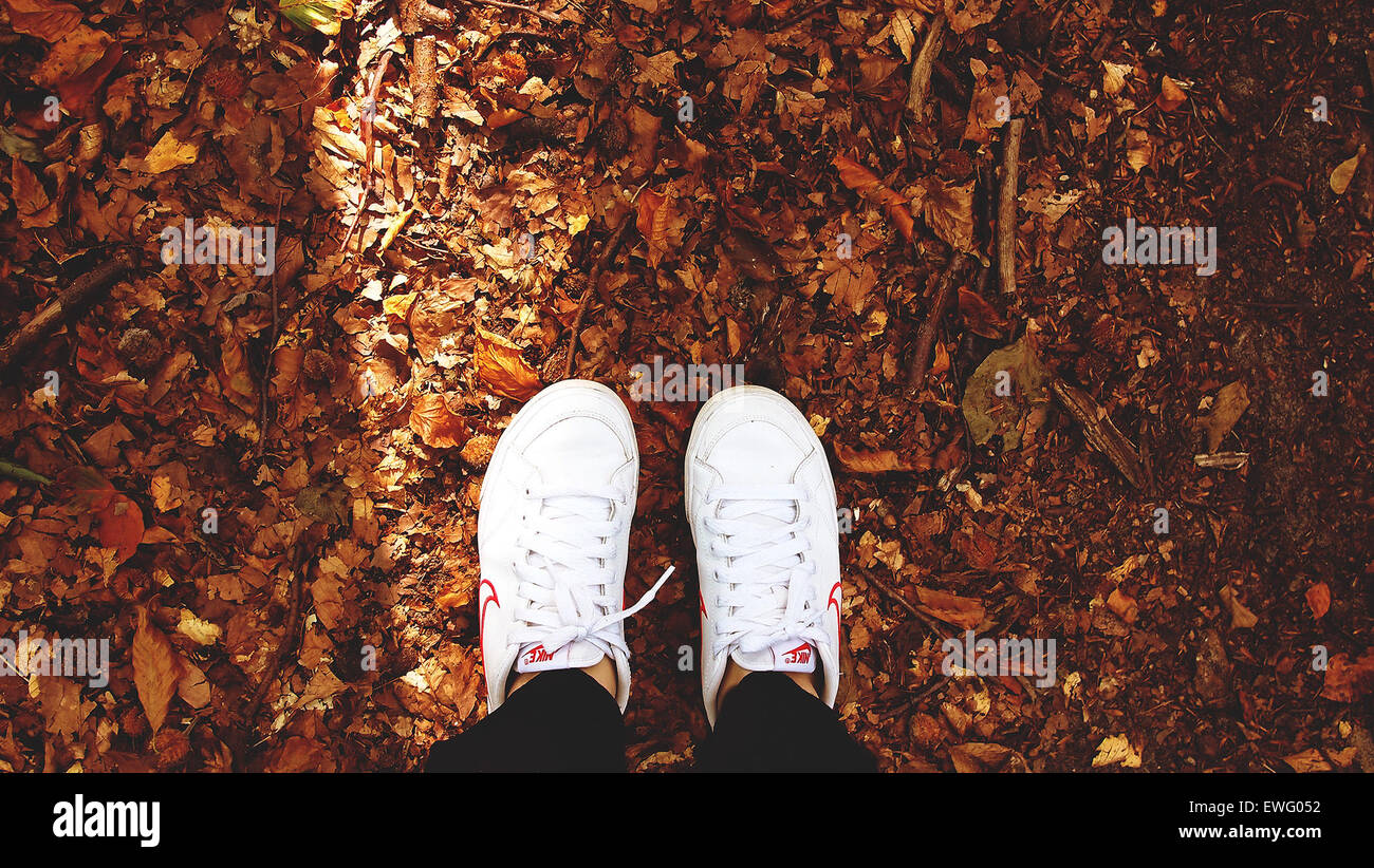 Two Feet in White Nike Sneakers Standing on Dry Leaves Stock Photo