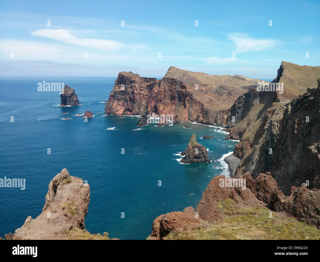 A stunning view of volcanic rock formations situated along the edge of the ocean. The jagged rocks stand out against the backdrop of the sea, with waves crashing at their base. The natural landscape highlights the contrast between the rocky terrain and the calm ocean. Stock Photo