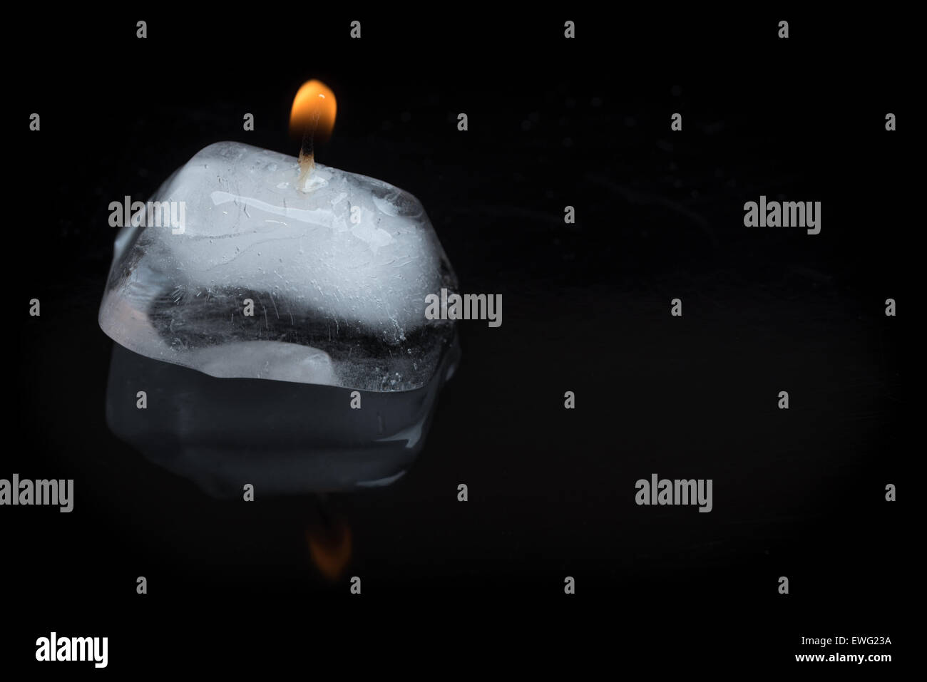 A close up shot of a lit candle wick stuck into an ice cube on a black background with reflection. Stock Photo