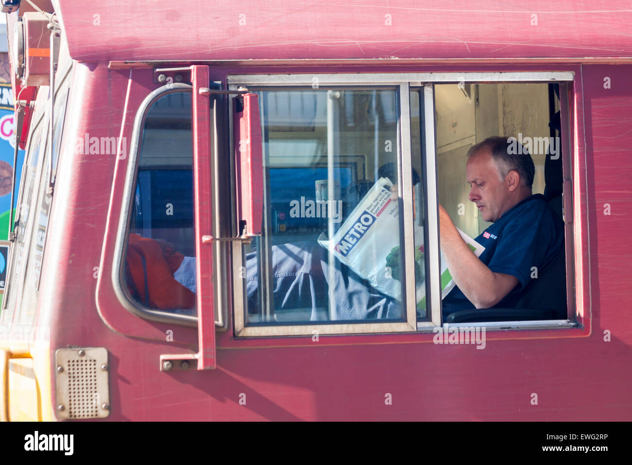Freight train driver in cab reading the Metro newspaper while train stopped at Southampton Central Station, Southampton, Hampshire UK  in June Stock Photo