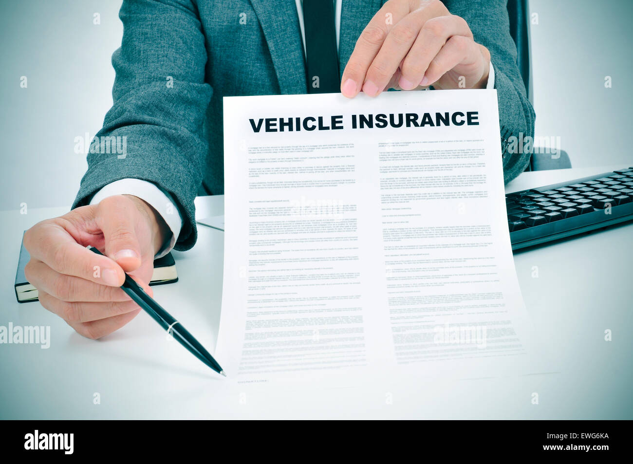 a young caucasian man wearing a gray suit in his office shows a vehicle insurance policy and points with a pen where the policyh Stock Photo