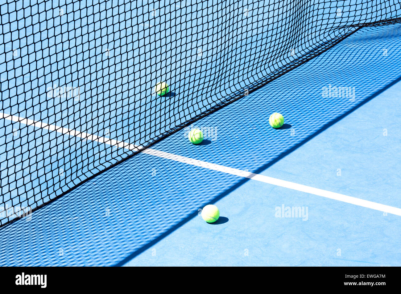 Blue tennis court with network and four yellow balls on the floor Stock Photo