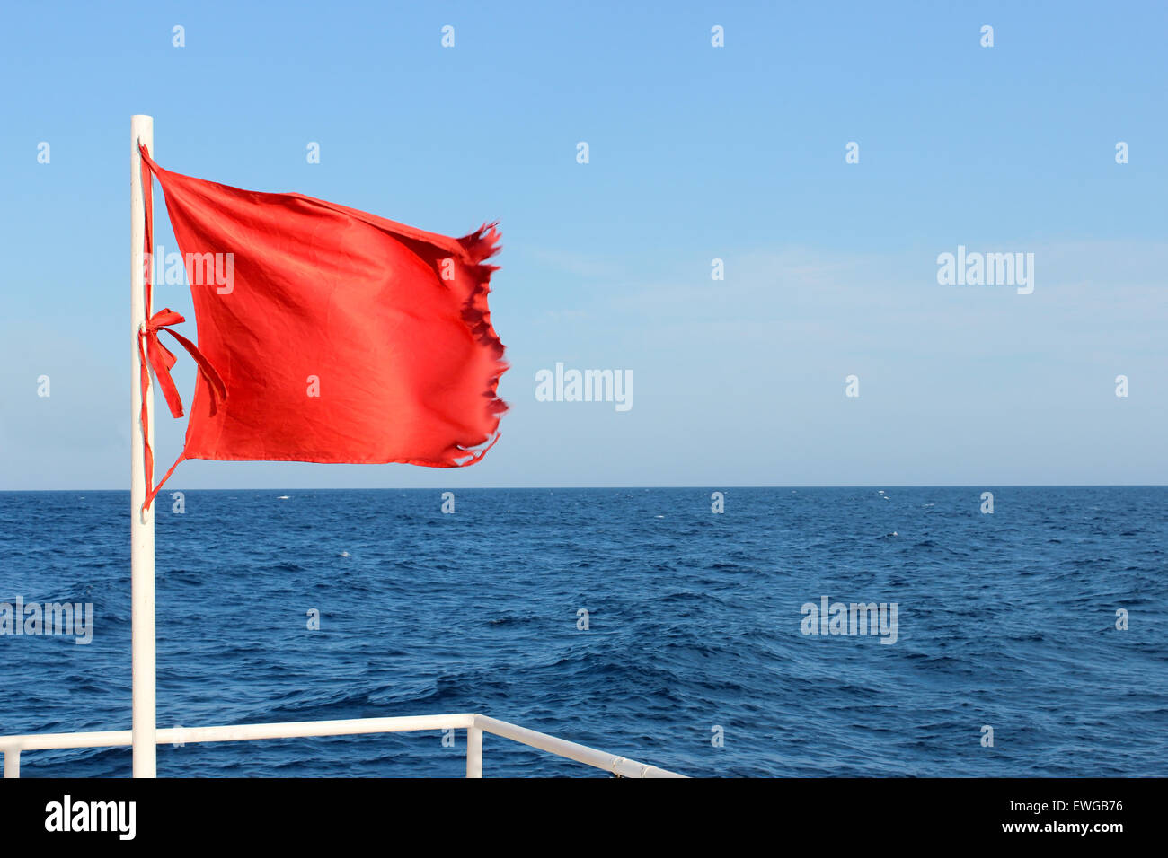 Red flag flying in the background of the sea, warning of the increasing wind and waves. Stock Photo