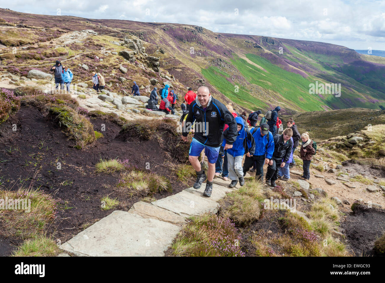 A large walking group. Walkers hiking on a stone path at the top of Grindsbrook Clough, Kinder Scout, Derbyshire, Peak District, England, UK Stock Photo