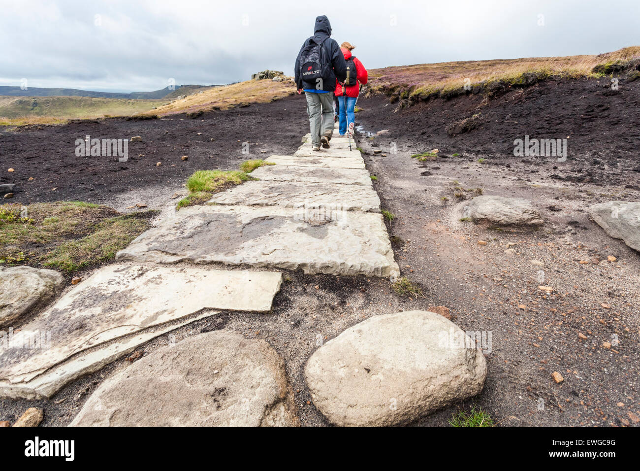 Moorland conservation. Walkers walking on a stone flag paved path on the moors of Kinder Scout, Derbyshire, Peak District National Park, England, UK Stock Photo