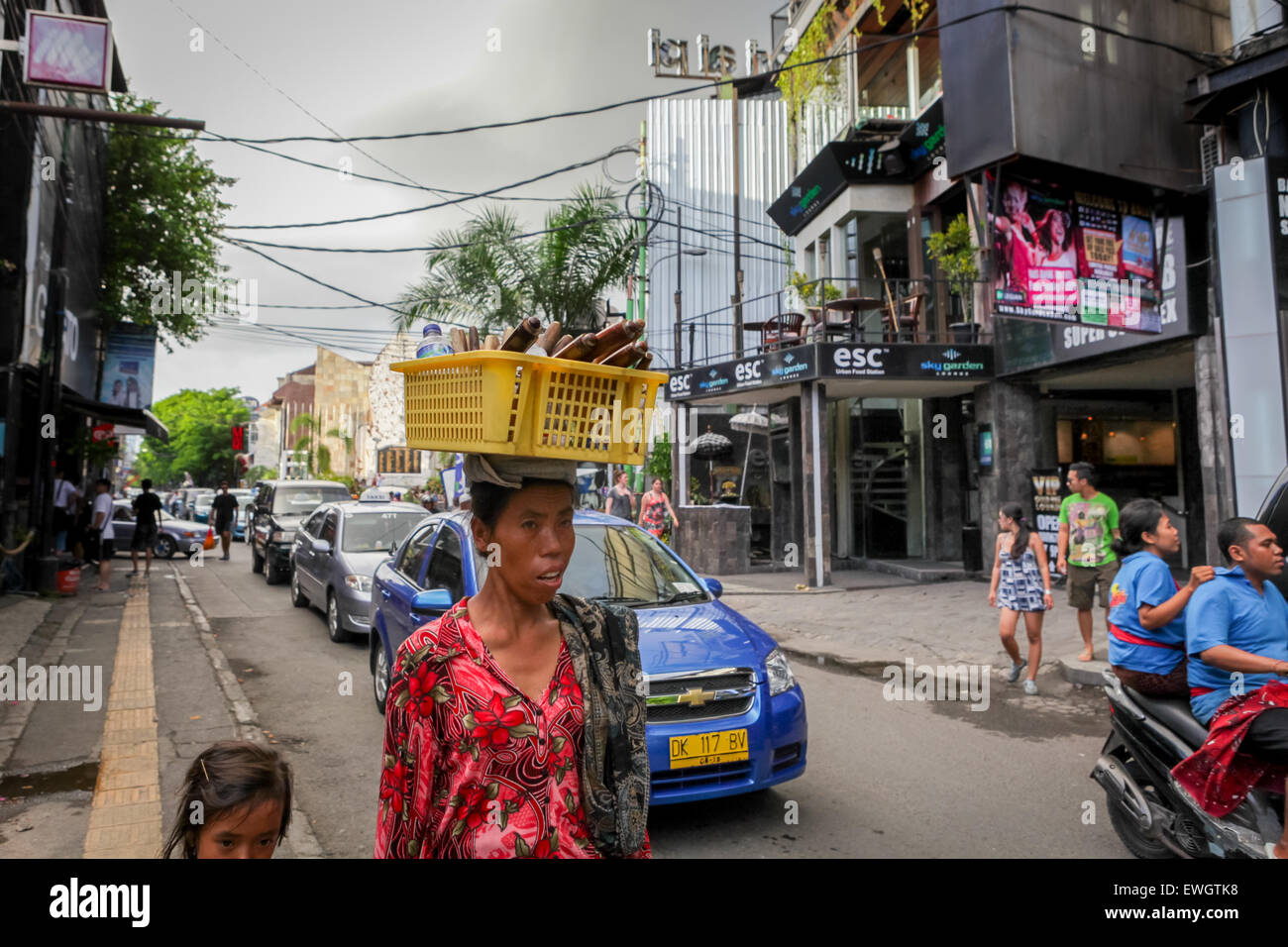 Balinese woman carrying crafts and water bottle on her head on Legian Street, Bali. Stock Photo