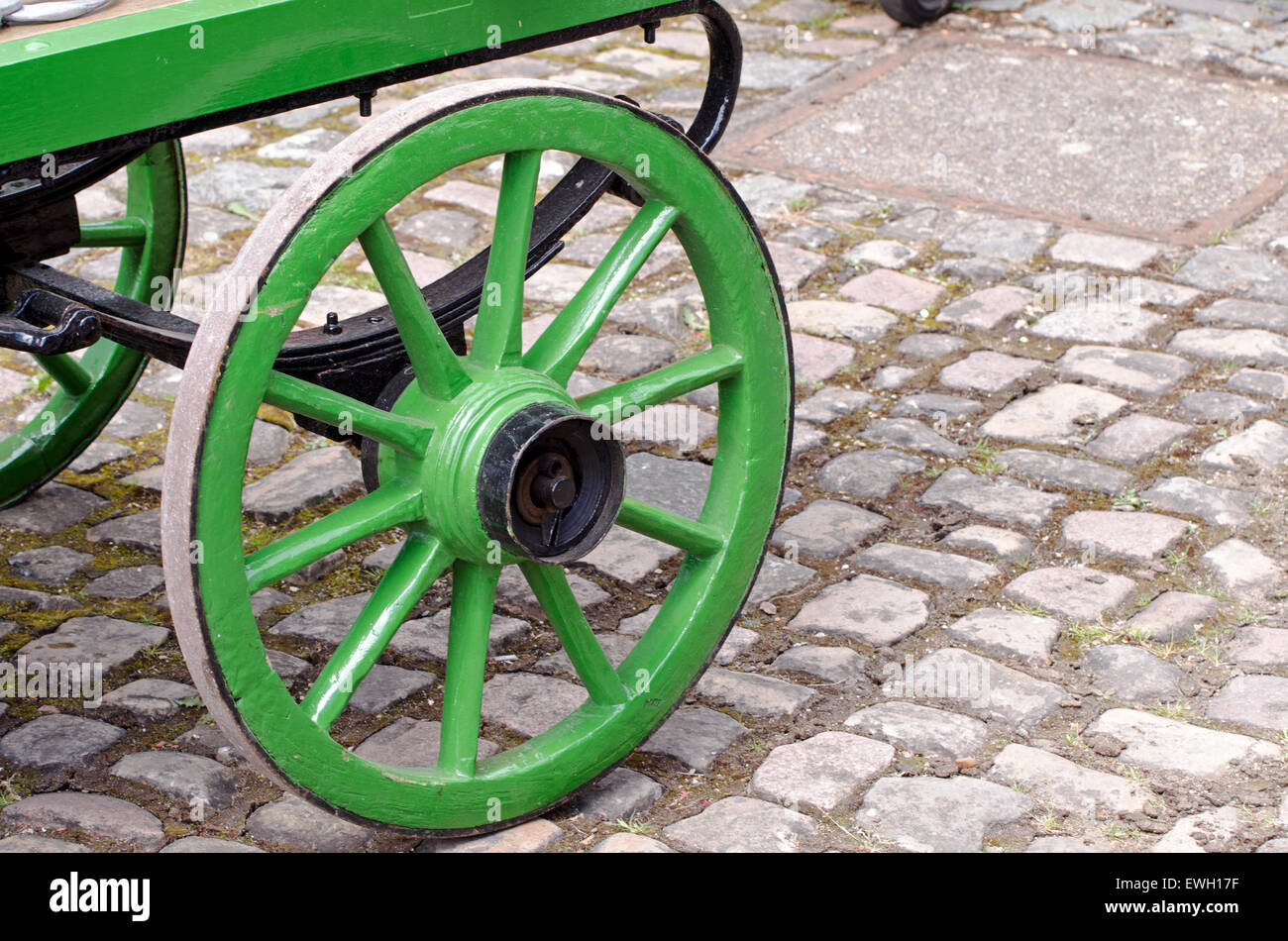 Wooden wheel and iron rim - detail of an old-fashioned wood and iron cart standing on a cobbled surface of granite setts. Stock Photo