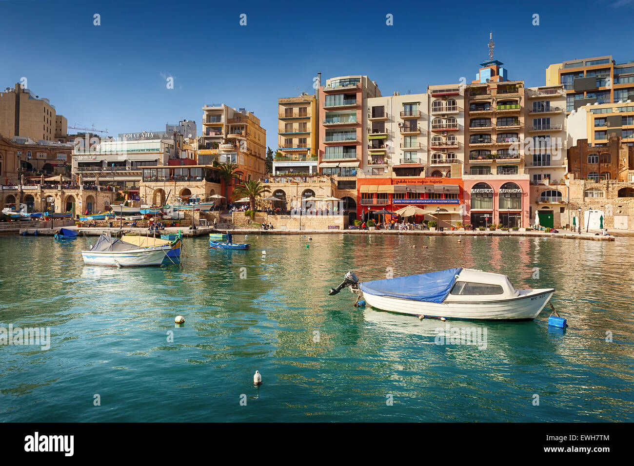MALTA - MARCH 22 2015: Spinola Bay with boats in front of famous touristic restaurants and Portomaso tower at back at St Julian, Stock Photo