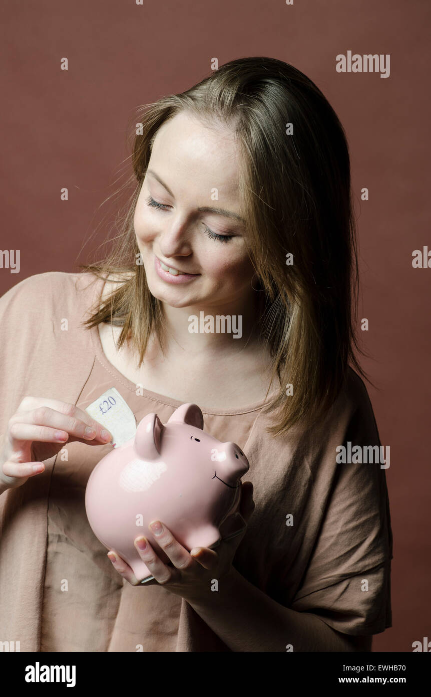 Young woman saving a twenty pounds Sterling note in a piggy bank Stock Photo