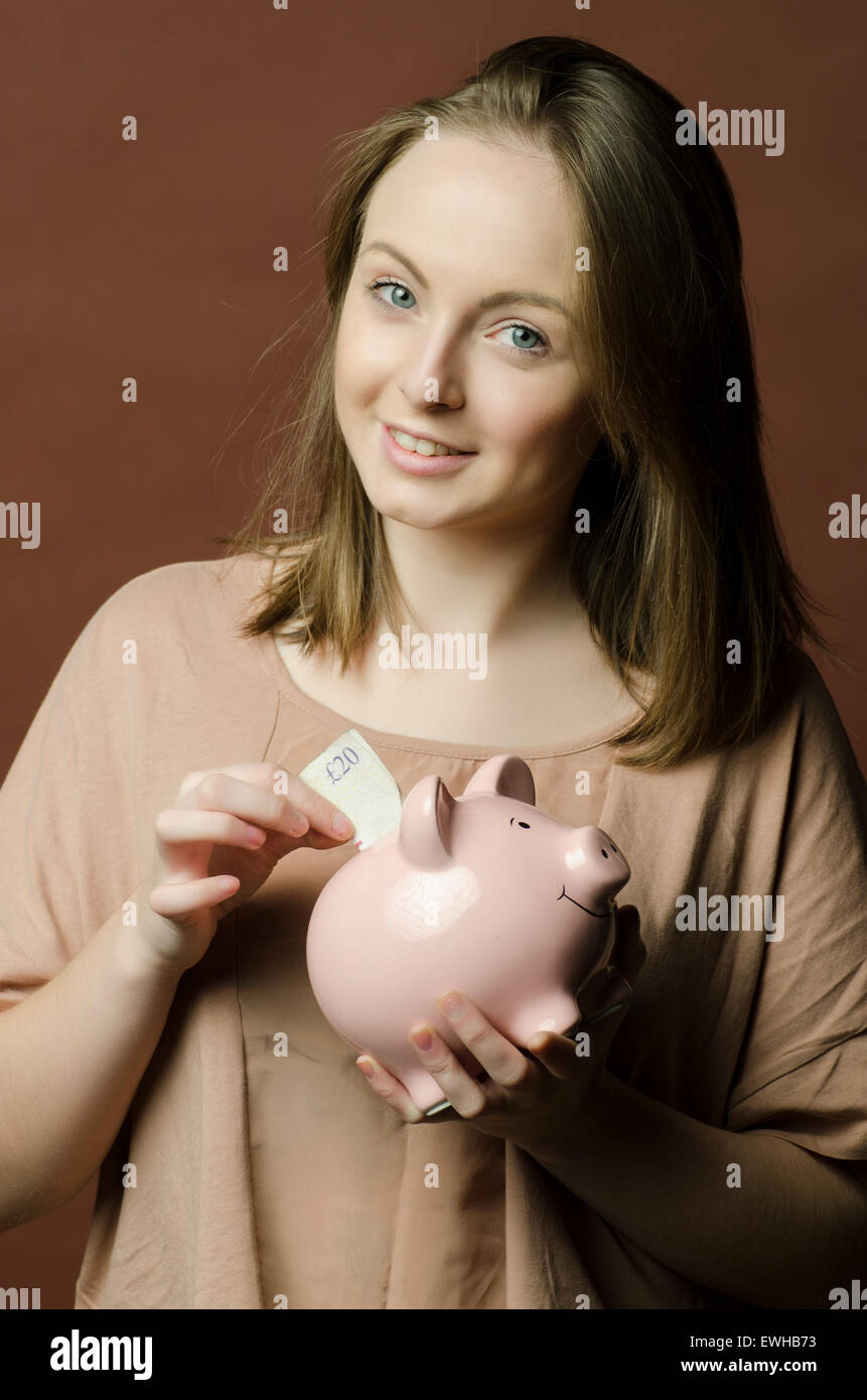 Young woman saving a twenty pounds Sterling note in a piggy bank Stock Photo
