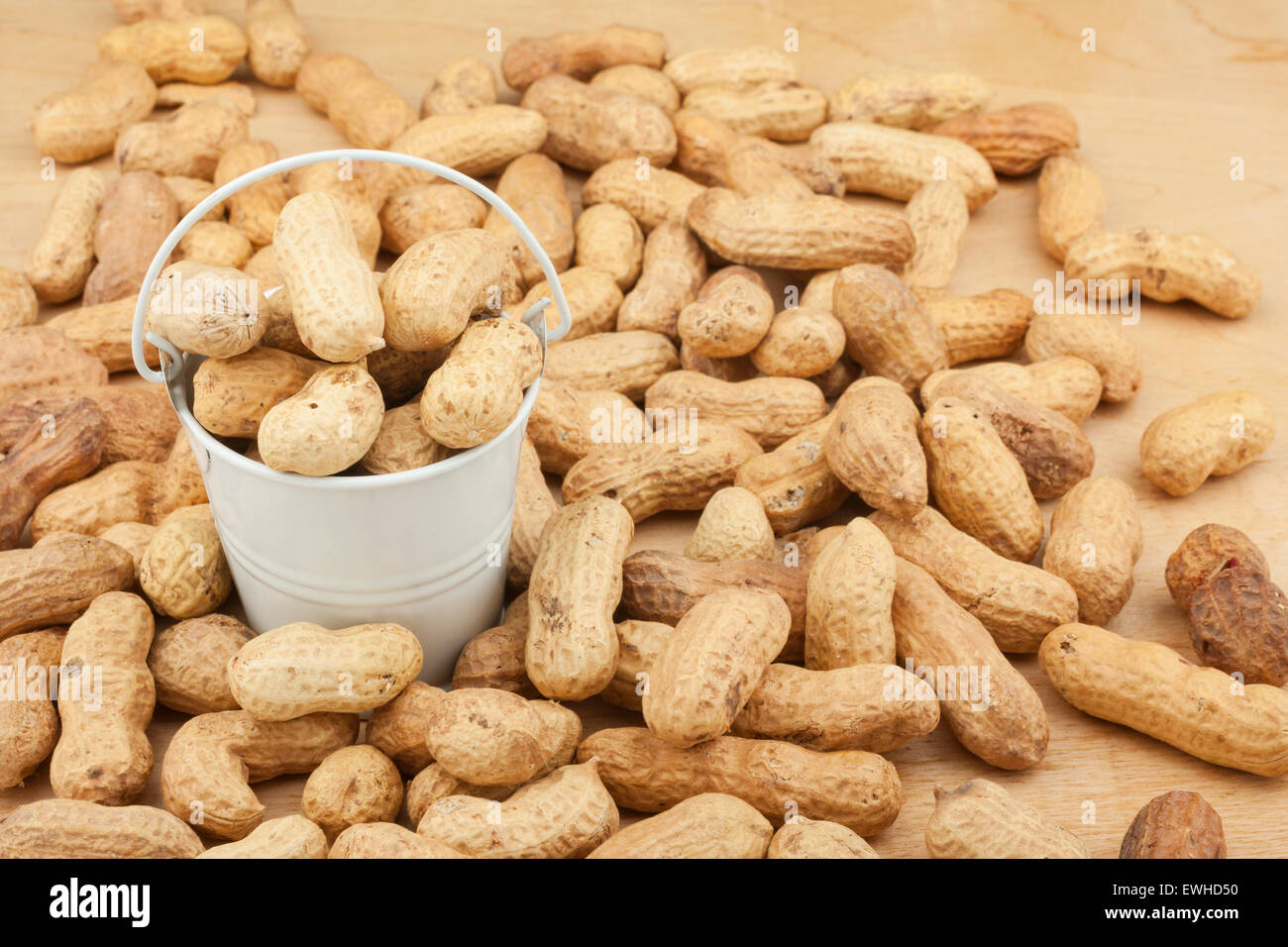 White bucket with dried peanuts on the wooden floor, as a background
