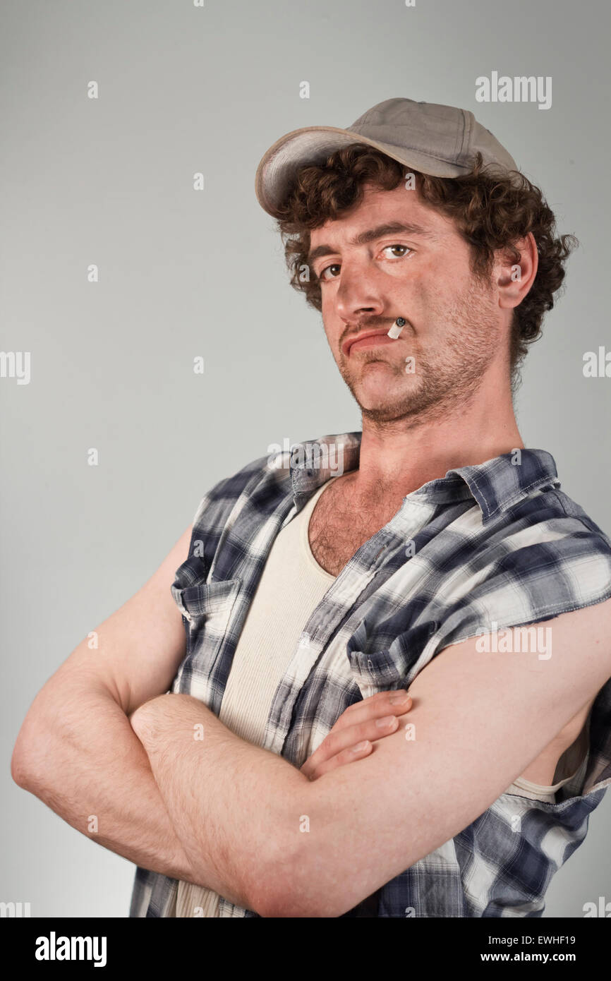 Confident redneck folds his dirty arms while smoking a cigarette Stock