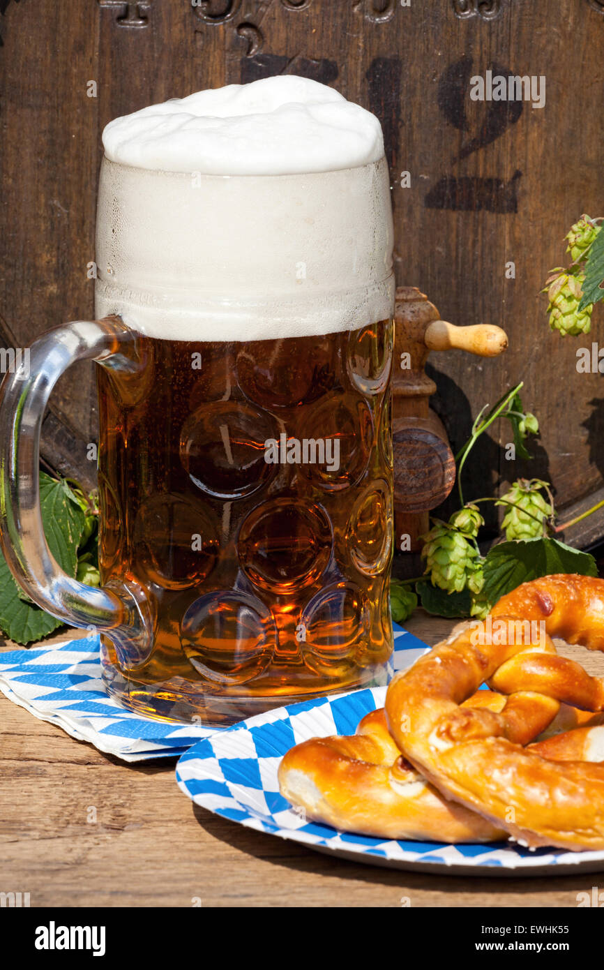 Beer barrel with hops, a large glass of beer and a pretzel on a paper plate Stock Photo