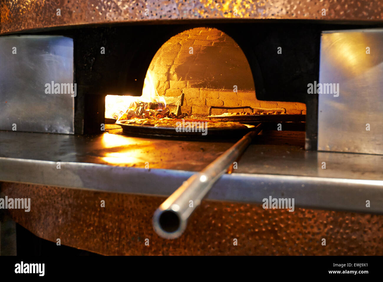 Traditional wood fired pizza being placed into a super hot brick pizza oven. Stock Photo