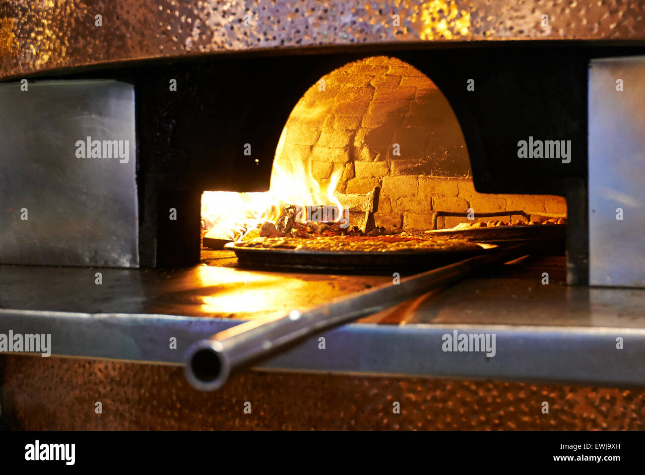 Traditional wood fired pizza being placed into a super hot brick pizza oven. Stock Photo