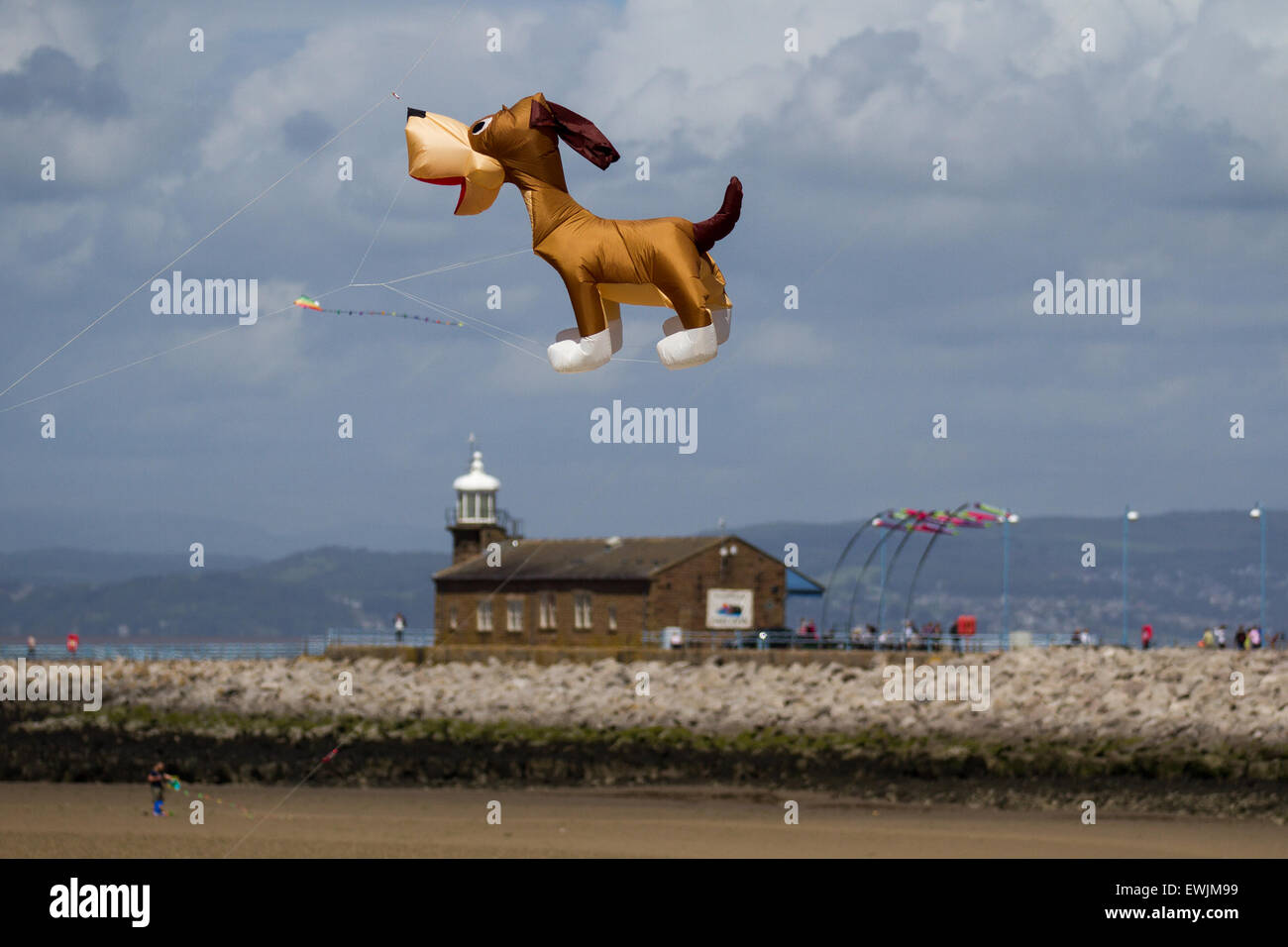 Big Inflatable comical cartoon dog flying over the Stone Jetty Light house in Morecambe. Catch The Wind Kite Festival an annual festival on Morecambe seafront, when for the whole day the skies are full of the most spectacular shapes, colours and flying creations.  Featured were animal kites of all kinds and sizes. Morecambe, Lancashire, UK June, 2015. Stock Photo
