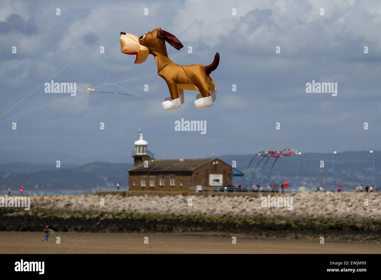Morecambe, Lancashire, UK 27th June, 2015. Inflatable comical cartoon dog flying over the Stone Jetty Light house. Catch The Wind Kite Festival an annual festival on Morecambe seafront, when for the whole day the skies are full of the most spectacular shapes, colours and flying creations. Featured were animal kites of all kinds and sizes. Stock Photo