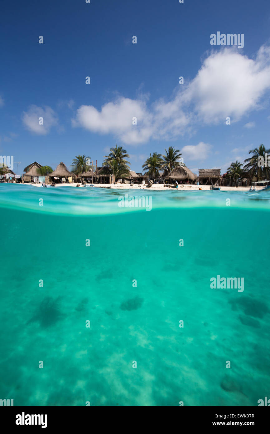 Above and below water of picture with thatch huts on tropical beach and tropical reef and white sand below Stock Photo