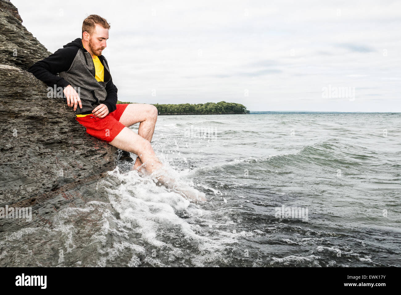 Young man sitting on a rocky cliff at a beach. Stock Photo