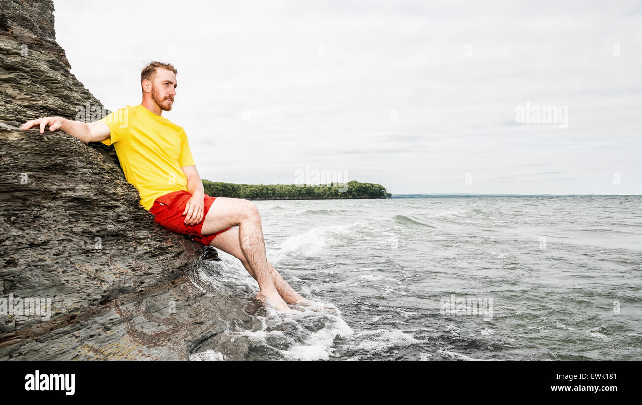 Young man sitting on a rocky cliff at a beach. Stock Photo
